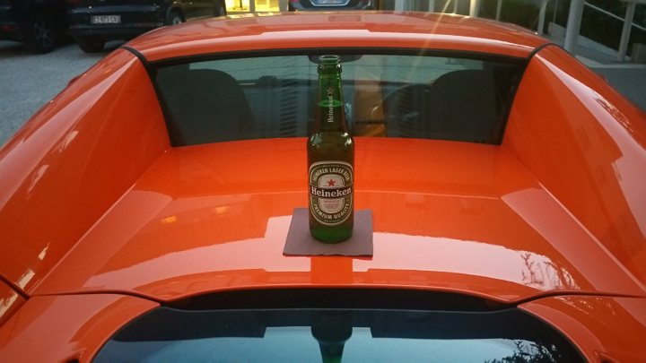 Car and Guitar solo road trip. - Page 3 - General Gassing - PistonHeads - The image shows the top of an orange, two-door sports car. A green bottle of beer is placed prominently on the car's sleek hood. The license plate bracket of the car is visible, suggesting a model like a classic VW Beetle. The background is a bit blurred, focusing the viewer's attention on the car and the beer bottle. The scene evokes a casual, relaxed atmosphere, possibly in a residential area or parking lot.