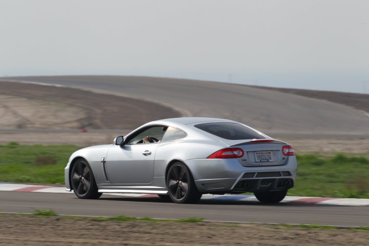 Pistonheads - The image depicts a dynamic scene on a race track. A gray sports car is in motion, captured from a low angle that accentuates its speed and the sense of movement. The car's wheels are turned slightly, indicating that it's navigating the curve of the track. In the background, the track curves to the left, with grassy areas beyond the confines of the race track. There are no other cars or drivers visible in the immediate vicinity of the sports car, emphasizing its solitary pursuit on the track.