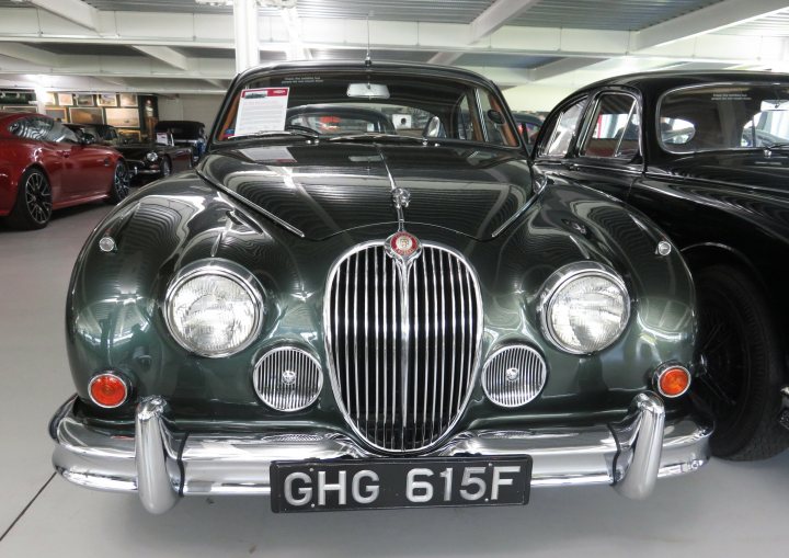 Pistonheads - The image displays a vintage car on display in an indoor setting. It appears to be a classic, possibly British vehicle, as suggested by the badge and design features. The car is shiny with a glossy finish, indicating it may be well-maintained or restored. There are other vehicles in the background, suggesting that this could be part of a larger collection or exhibition space. The car takes up a significant portion of the image, drawing attention to its condition and design.