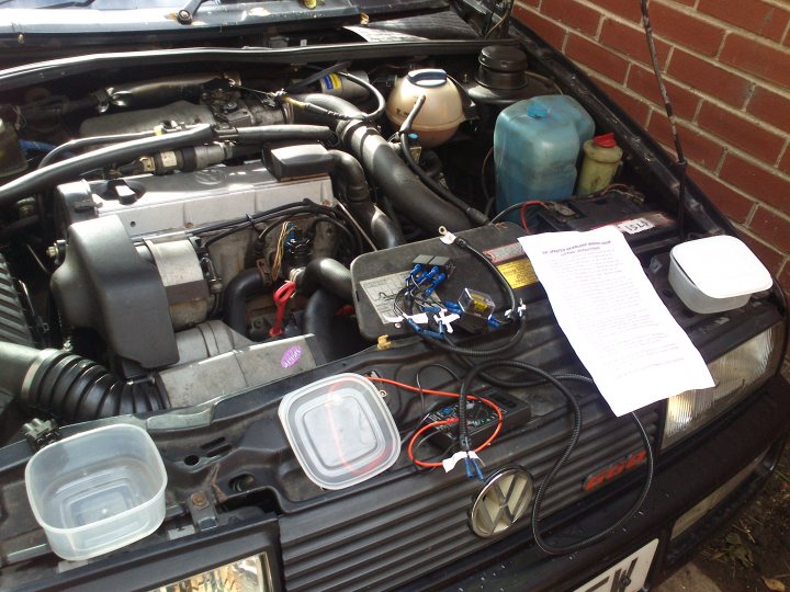 Volkswagen Corrado G60  - Page 3 - Readers' Cars - PistonHeads - The image portrays an open hood of a car, revealing its complex mechanical system. Various components such as black cords, a radiator, and a fuel system are visible, indicating possible repairs or maintenance being conducted. The background shows a brick wall, providing a contrasting setting for this mechanical view. A white piece of paper is placed on the engine, potentially containing instructions or notes for whoever is working on the car.