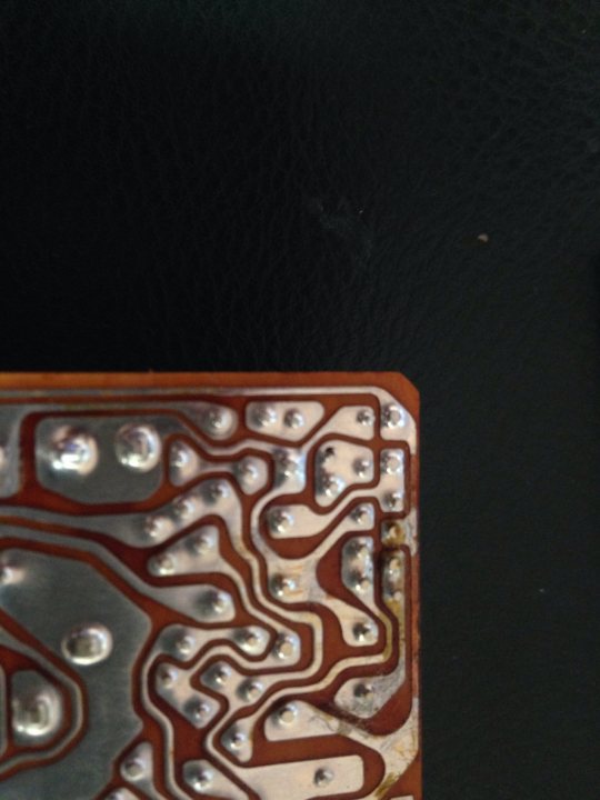 Electronic circuit board / relay repairs - Page 1 - Home Mechanics - PistonHeads - The image depicts a close-up view of a section of an electronic circuit board. The dominant color in the image is a metallic orange, which stands out against the darker background. The circuit board is composed of a series of interconnected pathways, some of which are etched with patterns and intricate designs. The surface of the board is dotted with those tiny silver bubbles, indicative of a soldering process. The overall texture of the board, despite the solder, shows signs of use and perhaps indicates the complexity of the electronic device of which this is a part.