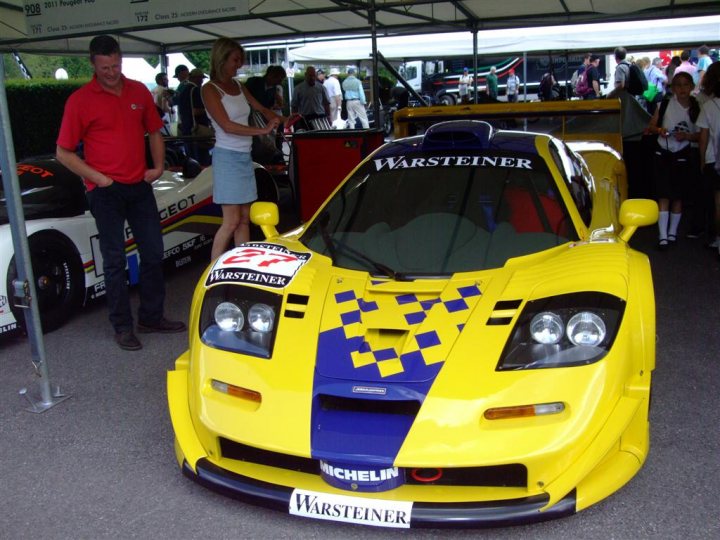 Goodwood FoS pics / videos - Page 1 - Goodwood Events - PistonHeads - The image showcases a yellow and blue race car with the number 52 prominently displayed. It's parked under a tent, where multiple standing people and chairs can be seen in the background, suggesting this might be an event or exhibition setting. The car features checkered patterns and the word "Wartsteiner" on the side, indicating it may be associated with the same racing team, though references to Michelin seem to currently show leading text. The overall context of the image is associated with motorsport events and car shows.