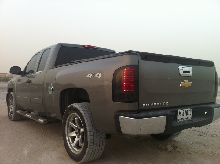 Not what  I had in mind but ....... - Page 1 - Yank Motors - PistonHeads - The image is a photograph of a vehicle that appears to be a Chevrolet Silverado pickup truck. The truck is painted in a light gray or silver hue and is equipped with a standard cab and short bed configuration. It has a chrome exhaust pipe and two tail lights on the back. There are no visible distinguishing marks or personalized modifications on the truck. The vehicle is parked on what looks like a flat, sandy surface, and the background is out of focus, possibly indicating a relatively open area. There is no text on the image, and the style of the photo is straightforward, capturing the truck from a side angle that showcases vehicles features.