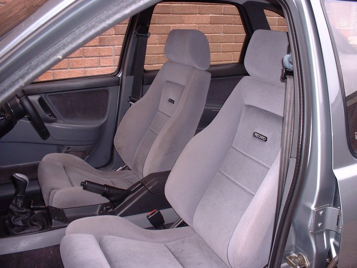 My Sierra XR4x4 Turbo Technics - Page 1 - Readers' Cars - PistonHeads - This is an image of the interior of a car, showing the passenger side of the vehicle. The car appears to be an older model, characterized by a gray interior with beige seats. On the driver side seat, there is a logo visible on the headrest, but the specific brand is not legible. The door has black handles, and the side mirror is not fully visible in the frame. The style of the image is straightforward, with no visible branding other than the logo on the seat headrest.