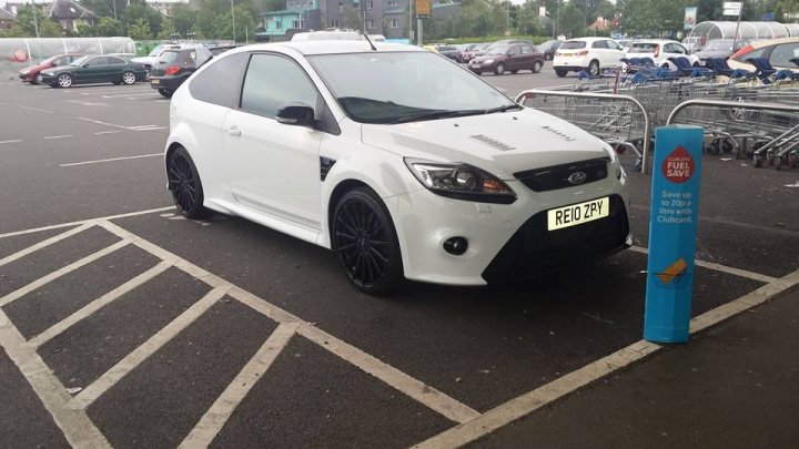 STOLEN : Edinburgh : Ford Focus RS - Page 1 - Scotland - PistonHeads - In the image, a white hatchback car is parked in a parking lot amidst a bustling scene of various cars and a bus. The car is positioned in a designated parking space, clearly identifying it as parking lot vehicle number BRE1ZP7A. Across the lot, a grocery store can be seen, suggesting that the car is likely parked on the outskirts of a shopping area. At the edge of the parking lot, a bright blue fuel post stands out prominently. Despite the flurry of activity, the white hatchback remains the focal point of the image. The photo seems to have been taken from a distance, possibly from another parking spot, capturing the scene in front of it. In terms of orientation, it's difficult to definitively determine whether the photo was taken from a high angle or from within another car. Overall, the image paints a common scene from everyday life.