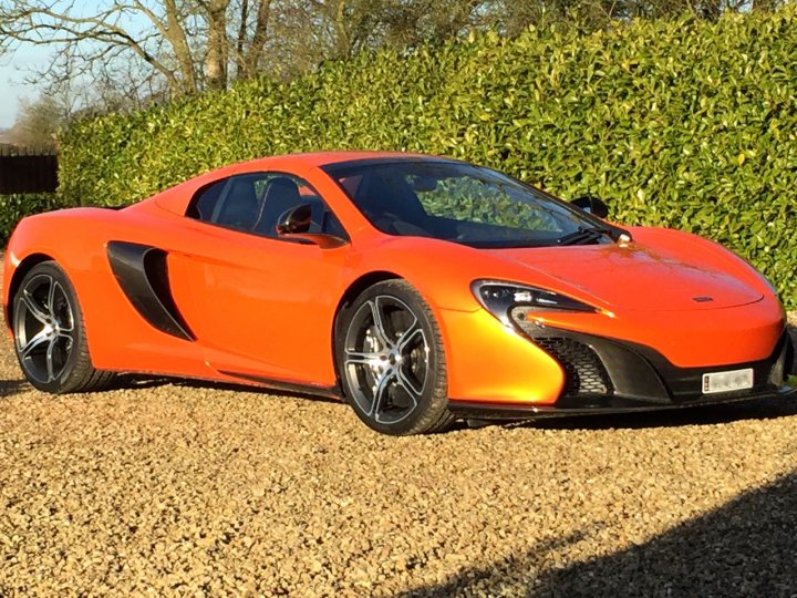 Time is dragging! - Page 1 - McLaren - PistonHeads - The image showcases a vibrant orange McLaren car parked on a pebbled surface. It's an open-top model, which gives it a sporty and dynamic appearance. The car is positioned to the left of the frame, with the sun slightly shining on its body, adding to its overall appeal. Adjacent to the car, a green hedge provides a natural contrast to the orange of the McLaren. The vehicle is clearly the focus of the image, and its placement on the pebbles adds an interesting texture to the scene.