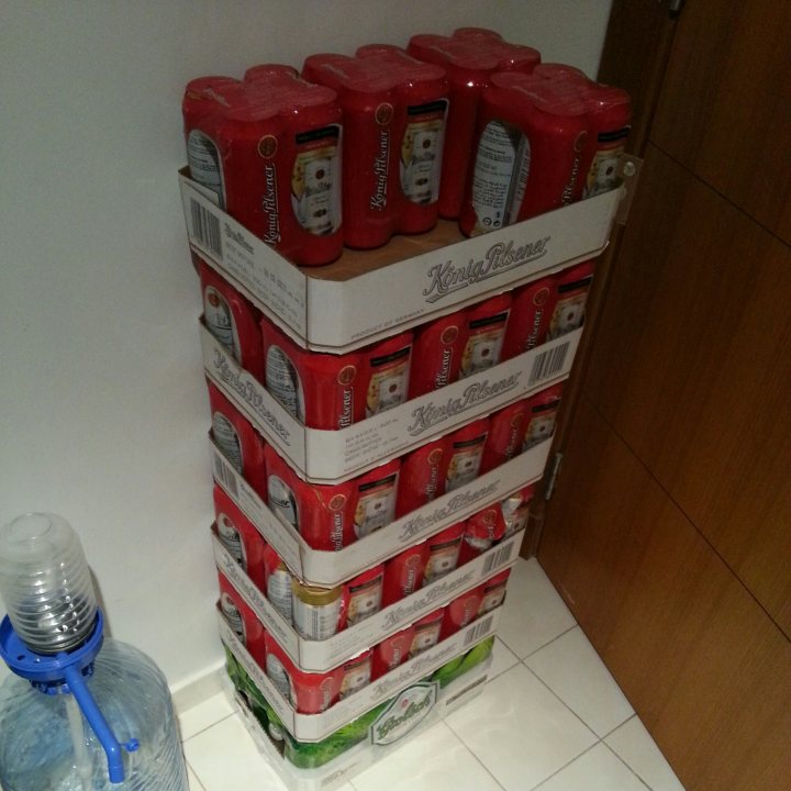 Pistonheads - This image showcases a collection of Kingfisher lagers, with a stack of red cans sitting on top of another stack. The red cans are positioned behind what appears to be a water dispenser, providing a vivid contrast. The cans are arranged in a sturdy metal rack, suggesting these are drinks intended for purchase or consumption at a convenient location. The overall setting, indicated by the backdrop, seems to be a public place, likely a shop or store.