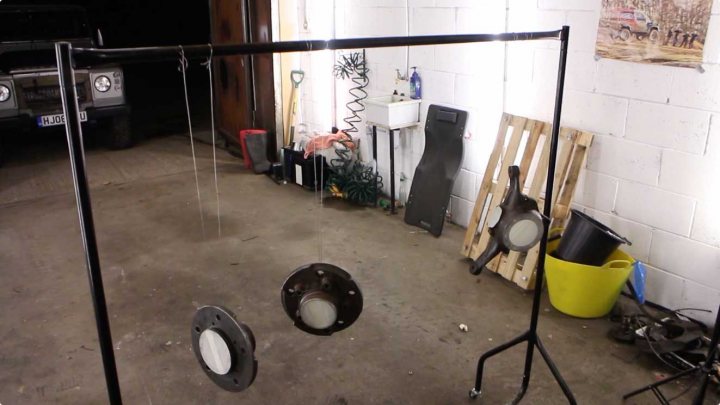 A kitchen with a refrigerator and a stove - Pistonheads - The image shows a garage setting with a clear focus on a metal object that appears to be a pole with three circular lights hanging from it, which could be part of an elaborate set-up or a DIY project. This pole is positioned next to two stands, each holding different objects. One stand holds what looks like a large pair of binoculars, and the other is supporting an off-white box with control knobs on it, possibly a pedalboard for a musical setup, given the numerous circular elements present. In the background, various household items can be seen, including a black backpack leaning on a white fridge-freezer, a yellow bucket on the floor, and a few other random items scattered around, suggesting a used and partially disorganized space. A glimpse of a car can be seen at the far left edge of the image, indicating that the garage might also serve as a parking area.