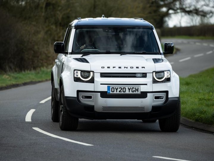 RE: 2020 Land Rover Defender | The short review - Page 1 - General Gassing - PistonHeads - The image is a photograph of a white SUV with a distinctive design, traveling on a road. The vehicle has a modern and sleek appearance, with prominent wheel arches and a large grille that houses the brand emblem. It's equipped with alloy wheels, and there are visible headlights at the front. The car is positioned in the center of the image, with the viewer looking slightly to the left, indicating movement along the road. There are no other vehicles or pedestrians immediately visible in the immediate vicinity, giving a sense of solitude. The road appears to be in a rural area as suggested by the absence of any urban structures and the presence of greenery in the background.