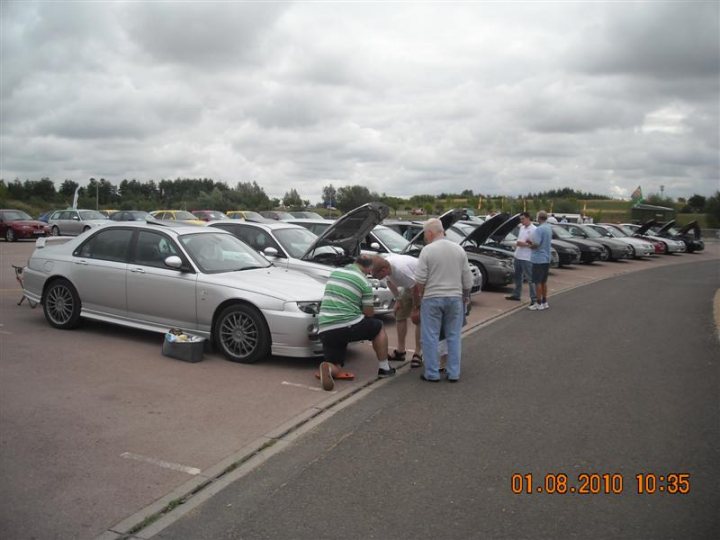 Pistonheads - In the image, two people are standing in a parking lot, engaged in a conversation. The parking lot appears to be in an urban setting, and there are several cars parked in an adjacent lot. A trunk is open on one of the cars, and one of the individuals seems to be inspecting something under the hood. The owner of the car is standing nearby, attentively listening to the conversation. The setting suggests that this could be a casual meeting or inspection of the vehicle.