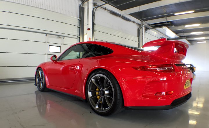 991 GT3 Prices  - 50 cars available! - Page 62 - 911/Carrera GT - PistonHeads - The image shows a vibrant red Porsche sports car parked inside a garage. The car is positioned diagonally, angled towards the right side of the photograph, with the driver's side closer to the camera. Its bodywork is sleek and glossy, reflecting the interior light of the garage. The garage itself has a white wall on the left side, and the interior is lit, creating a contrast with the red of the car. The image is a photograph and captures the car's dynamism against a static backdrop.