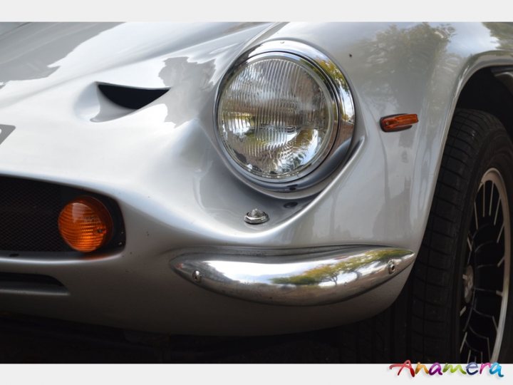 Early TVR Pictures - Page 36 - Classics - PistonHeads - The image showcases the illuminated headlight of a white classic vehicle. The headlight appears sleek and modern, suggesting a blend of old-world design with contemporary features. A side mirror and spoke wheel are visible, adding to the classic aesthetic of the vehicle. The background is blurred, drawing attention to the headlight and front grille. The lighting highlights the contours of the car, emphasizing the smoothness of its surfaces and the chrome detailing on the nose.