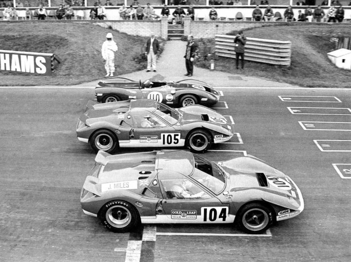 Lotus Europa 1966-1975 & tuning & conversions etc - Page 6 - General Lotus Stuff - PistonHeads - The image is a black and white photograph capturing a moment from a race at a track that appears to have the logos "HAMS" and "103" on it. Multiple young men are standing beside a series of race cars on the grid, waiting for the start of the race. Each car is labeled with the number thirty, represented by "30" on the side. The racing cars are classic in appearance, suggesting an older era of racing. The stands surrounding the track are occupied by spectators, adding to the atmosphere of anticipation and excitement before the race begins.