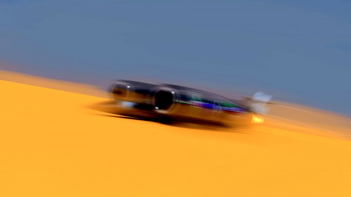 Bloodhound SSC Thread As Requested..... - Page 95 - General Gassing - PistonHeads - The image captures a moment of speed with a black car in motion, racing towards the viewer. The background is a blurred yellow, likely representing the road or a runway, with little details, focusing the viewer's attention on the car. The driver of the vehicle is not visible in the frame. The motion of the car is conveyed through the blurred lines around it, giving a sense of speed and movement.