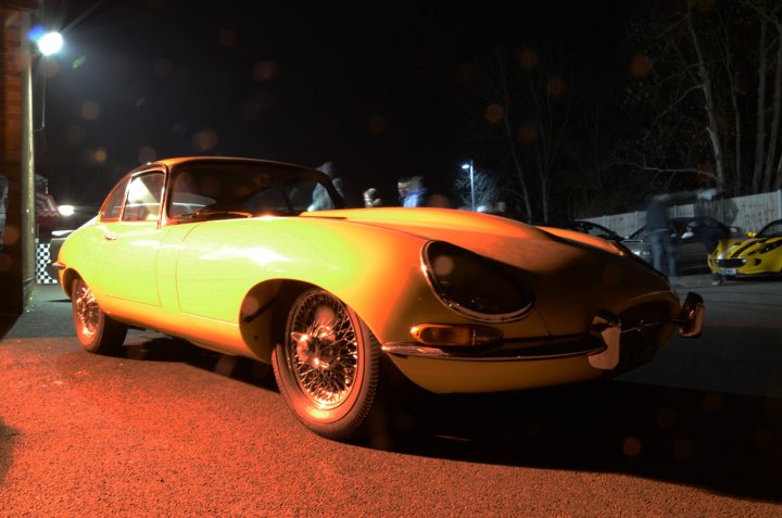 Essex March Pistonheads - The image captures a dynamic scene at a suburban house at night. The main focus is a beautifully restored, two-door sports car parked in the driveway. Its vibrant, metallic gold color shines under the ambient light, accentuating its sleek design and the chrome details around the windows and headlights. 

The car's headlights pierce through the emptiness, casting a warm glow that contrasts with the dark surroundings. The yard is adorned with a few sparse trees, standing tall and silhouetted against the moonless sky. 

Another car is visible in the distance, but it is smaller and less prominent than the proudly exhibited sports car. The atmosphere is quiet and still, with the absence of people or significant activity. The serene scene evokes a sense of anticipation, perhaps for a journey or an event to come.