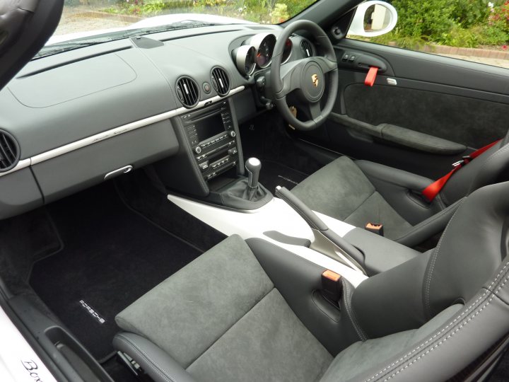 Buying Pistonheads Boxster Spyder - The image showcases the interior of a shiny gray Porsche car. The car is parked outdoors and seems to be in pristine condition. The car's dashboard and control knobs are on the left side of the dashboard. The steering wheel and various controls are neatly arranged. In the driver's seat, a single orange car key stands out, next to a red scarf adding a touch of flair to the scene.