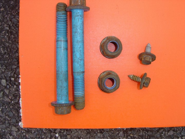 Pistonheads - The image displays a collection of used or worn parts laid out on an orange background. These parts include a set of threaded inserts with twisted blue ends, a larger threaded insert with a blue cylindrical top, and a smaller component that appears to be a metal screw with a tapered top. The focus of the image is on the metal components, suggesting the wear and use these parts have undergone. The image is likely taken to document the condition of these components, possibly for a repair project or to convey their utilitarian nature.