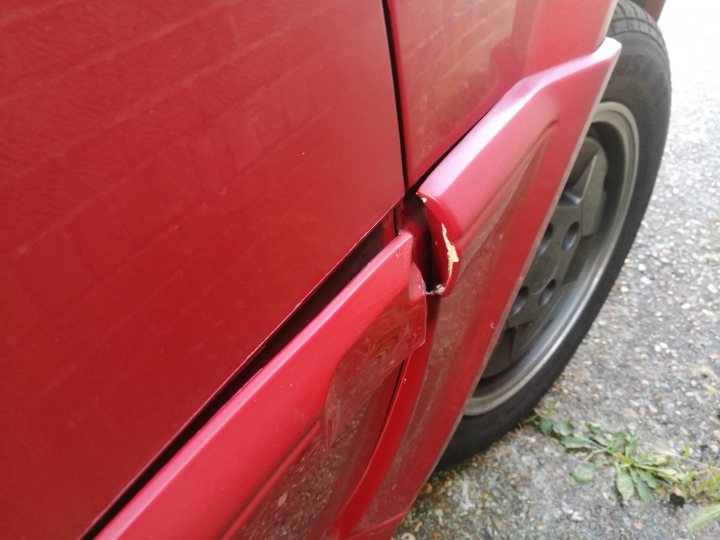 My bodged Citroen BX 16v - Page 12 - Readers' Cars - PistonHeads - The image shows a close-up of a red rear fender of a car parked on a paved area. The fender appears slightly chipped and scratched, indicating it might have been in contact with rough surfaces or suffered minor damage. There are visible tire-related textures, including a white wall tire and a black tire. The background is indistinct, focusing attention on the vehicle.