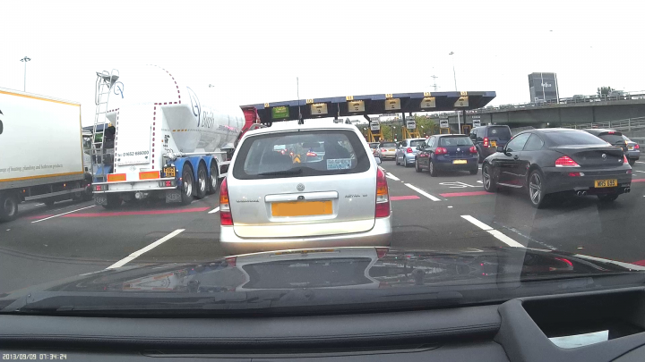 Why do people put "M" badges on non-M cars? - Page 52 - M Power - PistonHeads - The image shows a busy highway filled with a variety of vehicles. A silver car is positioned close to the camera at the front of the line. Further back in the traffic is a white truck with a large storage compartment, taking up a significant part of the lane. In the distance, multiple cars of different colors can be seen. The vehicles appear to be at a standstill, suggesting a traffic jam. The background is clear, with no other notable landmarks other than the road and vehicles.