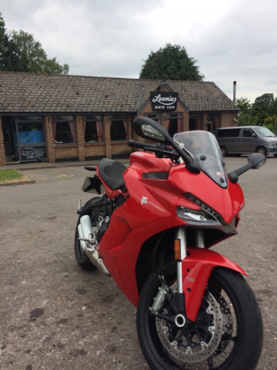 A picture a day....biker banter (Vol 4) - Page 451 - Biker Banter - PistonHeads - The image shows a striking red Ducati motorcycle parked on the side of a street in front of a building with the sign "Dominos Pizza". The motorcycle is sleek, featuring a design typical of Ducati, and it has a large windscreen. There are a few other motorcycles in the background, and a gray van is visible on the far right. The sky above is overcast, indicative of a cloudy or possibly rainy day.