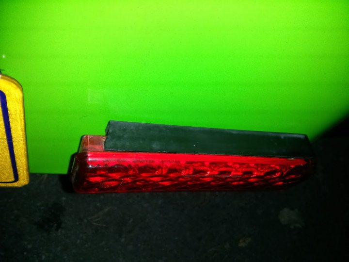 A piece of luggage sitting on top of a wooden bench - Pistonheads - The image shows a close-up of a red automotive brake light against a bright green surface. The brake light is rectangular with a textured casing. The colors red and green contrast sharply, with the red appearing vibrant and the green being a vivid hue. There are no visible texts or branding on the object. The light is situated in the foreground, with varying levels of focus, giving depth to the surface.