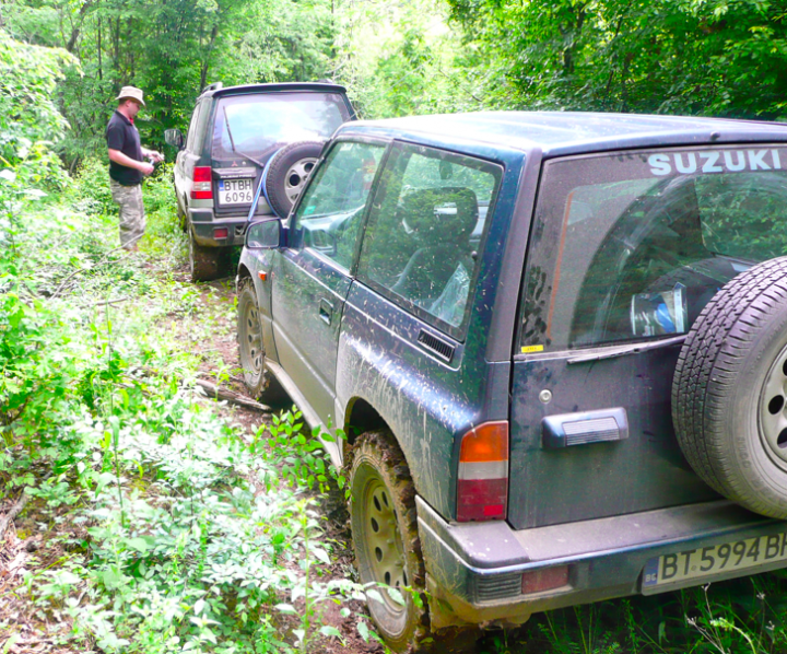 Little overnight trip to the Balkan range - Page 1 - Off Road - PistonHeads - In the image, two white Suzuki brand trucks are seen driving along a muddy dirt road. The trucks have a classic design, with the word "SUZUKI" prominently displayed on the side. In the scene, a person wearing a black shirt is standing next to one of the trucks, while the other truck is close by. The road is flanked by vibrant green trees, creating a lush backdrop for the vehicles. The presence of the person and the trucks suggest that they might be on a journey or adventure.