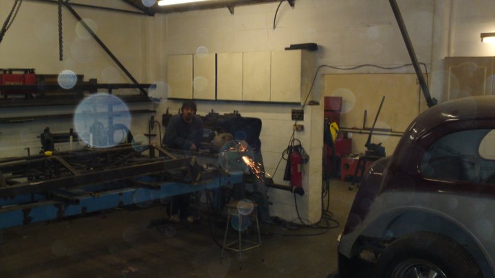 Dual Suspension Recumbent??? - Page 2 - Pedal Powered - PistonHeads - The image captures a bustling scene inside an auto workshop. A man dressed in dark clothing is standing by a large metal object, possibly working on a project. There's a noticeable presence of industrial equipment nearby, including a red and yellow object and a black bench. The surroundings are characterized by large white metal walls, a crucial part of the workshop environment, and a brown car parked nearby, possibly awaiting repair or maintenance. The cameraman's reflection, along with their shadow, can be seen on the car, adding a personal touch to this professional setting.