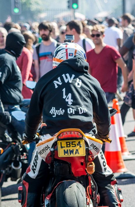 NWB Ryde or Die: what's it all about? - Page 1 - Biker Banter - PistonHeads - The image captures a dynamic scene of a crowd of people, with the event captured being a motorcycle race. At the forefront, a motorcycle is prominently displayed, bearing the number 14 and the political slogan "Ryde for Die". The motorcycle is being ridden by a person dressed in biker attire. Behind the rider, other individuals are scattered, each seemingly engrossed in the event. The setting appears to be a city street, indicated by the presence of traffic lights, one of which is clearly visible in the image. The overall atmosphere suggests an event filled with energy and adrenaline.