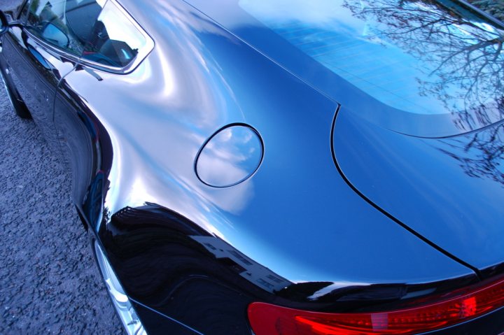 Pistonheads - The image displays a close-up view of a vehicle's rear section, showcasing a part of the bodywork. The car's shiny surface reflects a clear sky with some clouds, indicating a bright day. The reflection from the shiny metallic surface shows a building or architectural structure, suggesting the car is parked in a city area or near a commercial or residential complex. The overall textures, primarily the car's sheen, dominate the foreground, and the reflection of the sky adds a contrasting element. The lighting highlights the glossy finish of the vehicle's exterior.