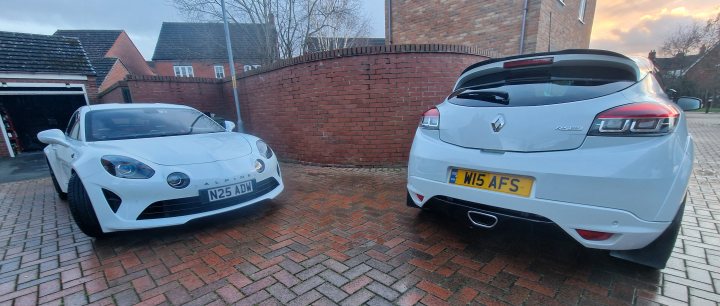 New Car Day Tomorrow - with a rail strike enforced twist - Page 2 - Readers' Cars - PistonHeads UK - The image shows two cars parked in a driveway. On the left is a white sports car, which appears to be a Nissan GT-R based on its design and badging. To its right is another vehicle that seems to be a hatchback with a unique body kit and custom modifications, including a spoiler and exhaust pipes visible at the rear. The cars are positioned side by side, indicating a comparison or showcase of their features. There's no text present in the image.