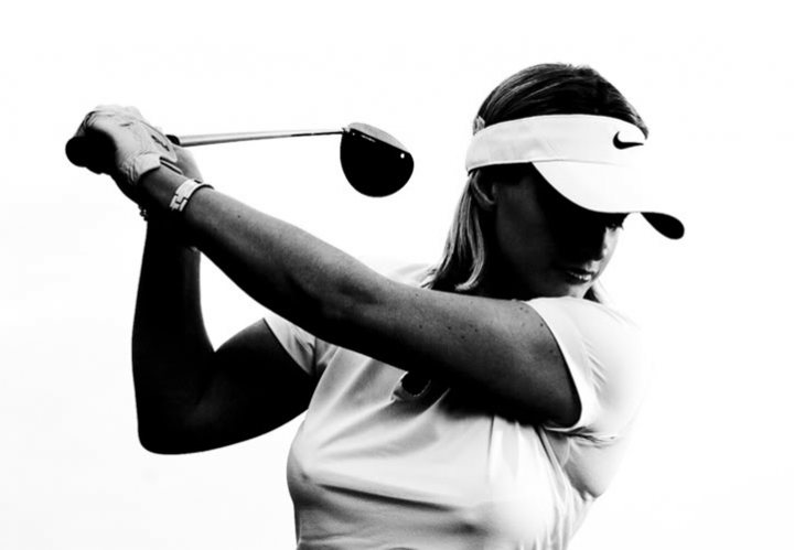 Sky Sports Golf presenter - Page 1 - Sports - PistonHeads - The image is a black and white photograph capturing a moment of action. It features a woman, presumably a professional golfer, mid-swing holding a golf club. She is dressed in a white shirt and sports a white visor. Her muscles are visible, indicating the intensity of the game. The woman's expression and body language convey a sense of concentration and focus. The background is minimalistic, drawing attention to the central figure and her sport.