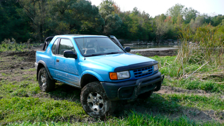 Towing/recovery with a Defender... - Page 1 - Off Road - PistonHeads - The image features a light blue pickup truck parked in a natural setting. The truck has large off-road tires suitable for navigating rough terrain. It is equipped with a winch at the front, indicating it might be used for towing or off-roading. The truck is parked on a grassy area with a forest edge in the background, and there is a stream visible to the right. The day appears to be slightly overcast, with the lighting rich and diffused, suggesting it might be an overcast day.