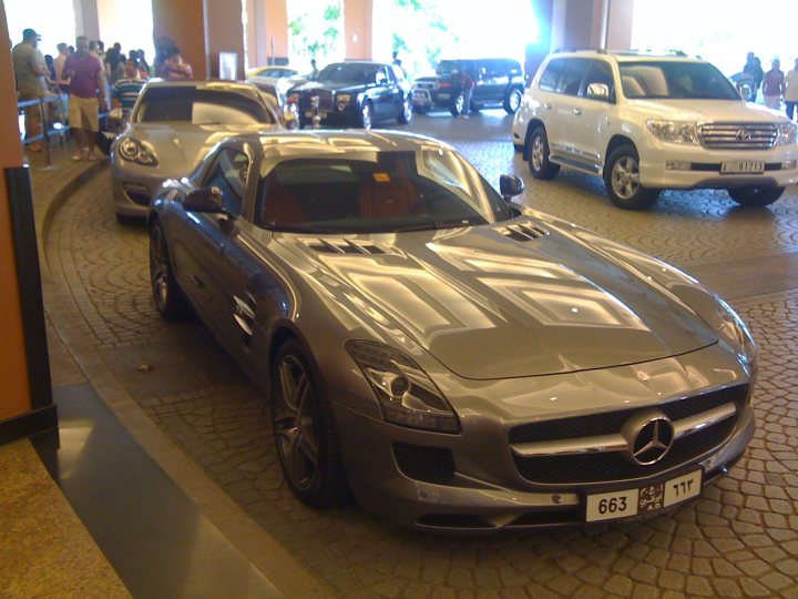 SLS AMG - Page 1 - Middle East - PistonHeads - The image captures a scene from a parking garage, where a variety of vehicles are parked in a neat row along a curve. The most prominent are a pair of luxury cars, one a Mercedes, parked amidst other models. The lot is well-lit, suggesting it's in an urban environment. People can be seen walking through the garage, adding life to this architectural backdrop. The precise positioning of the cars, along with the layout of the garage, gives a sense of order and tranquility in the image.