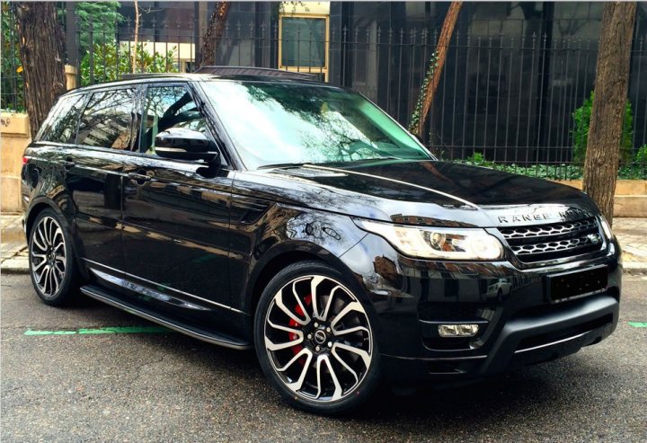 A black and white cat sitting on top of a car - Pistonheads - The image shows a modern-looking black crossover SUV parked on a road. The SUV has a sleek design with a prominent front grille and a set of large, black-rimmed wheels. There are no special plates visible on the front or rear of the car. The environment suggests an urban setting, with a building and trees visible in the background. The car appears to be in good condition with a glossy exterior.