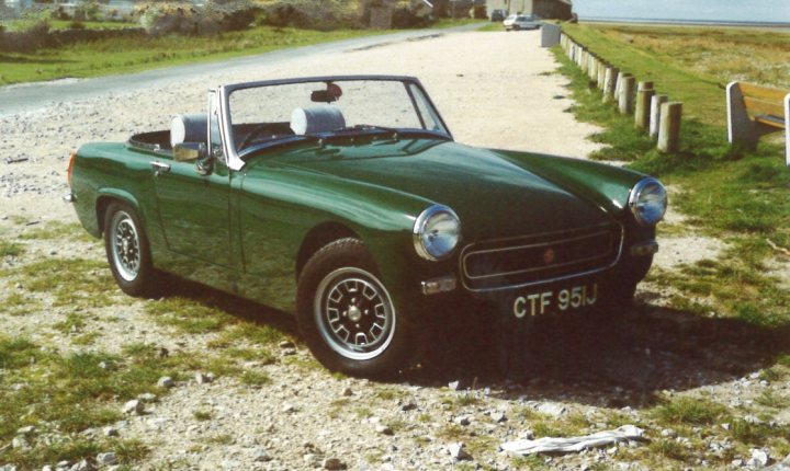 I want a classic mini, but... - Page 1 - Classic Cars and Yesterday's Heroes - PistonHeads - The image shows a vintage convertible car parked on a gravel road. The vehicle is painted in a glossy green finish and is the central focus of the image. The car has the top down, revealing its interior. The setting appears to be a rural or countryside area, with a grassy area and what seems to be a fence in the background. The weather appears to be clear, and the lighting suggests it could be late afternoon or early evening.