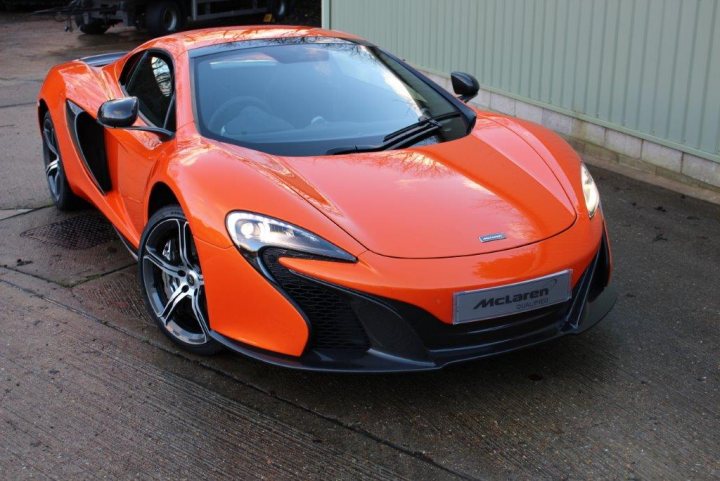 650S Spider Appreciation Thread - Page 1 - McLaren - PistonHeads - The image shows a vibrant orange McLaren sports car parked outside on a grey asphalt surface. Its sleek design features a long hood and a short rear deck, characteristic of the brand's high-performance vehicles. The vehicle has a prominent front grille with the brand's logo and a retractable hard top feature. The ambient lighting suggests it might be late afternoon. The McLaren is stationary, and there is a truck parked nearby in the background.