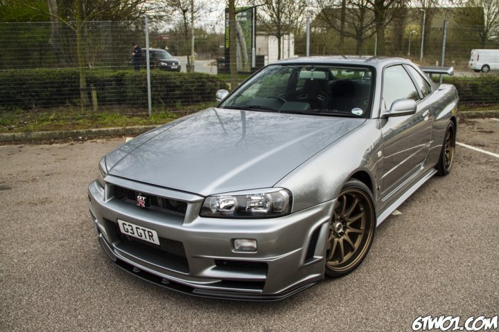 Nissan GTR R34 Nismo... what? - Page 1 - Jap Chat - PistonHeads - The image showcases a silver GT-R sports car parked on a concrete surface with a chain-link fence in the background. The car is in focus, highlighting its sleek and polished design. The name and logo of the proud owner, 'EXTENDED', are prominently visible on both the bumper and side of the car. It appears to be a sunny day, given the clear visibility and shadows cast on the ground.