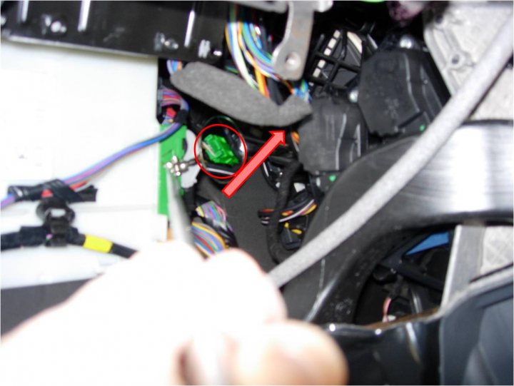 A pair of scissors sitting on top of a table - The image shows an open car dashboard with various components and wires exposed. A person's hand is seen holding a red object, which appears to be a tool or a part of the disassembled dashboard. The interior lighting illuminates the intricate workings underneath the dash panel. The background is slightly blurred but seems to be a garage or workshop setting. The dashboard is equipped with multiple screens and buttons that are typical of modern vehicles.