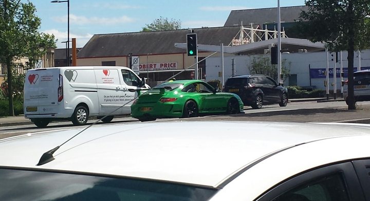 Spotted In South Wales (Vol 3) - Page 213 - South Wales - PistonHeads - The image is a composite of two photographs, one on top and the other below it. At the bottom, there is an overturned car with its roof open, revealing what appears to be a green interior. In the background, there are several cars parked along a street, and a truck can be seen in front of a building. There's also a traffic light and some pedestrians visible. The top photo shows a clear view of a road where a few cars are moving or parked. Both images seem to have been taken from the perspective of someone inside a car on this busy street, given the angle of the photos.