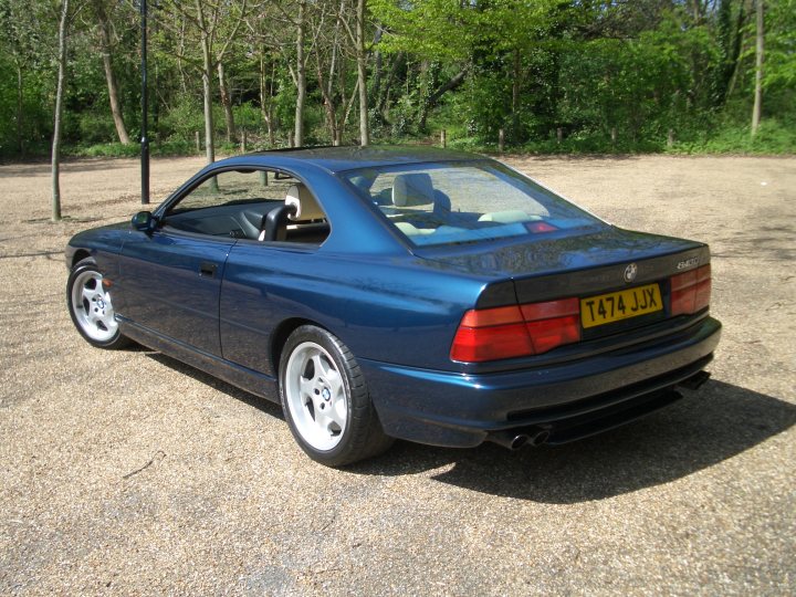 Jag XKR and BMW 840Ci - Page 7 - General Gassing - PistonHeads - The image depicts a lightly used, matte blue convertible sports car parked in a gravel lot. The car is at an angle to the camera with the front passenger side fendre most visible. The vehicle features alloy wheels and a European-style license plate that seems to say T44 JX. A large body of water can be seen in the background, indicating the car is parked near the water's edge. The foliage suggests that the photo may have been taken during an earlier season, possibly late winter or early spring.