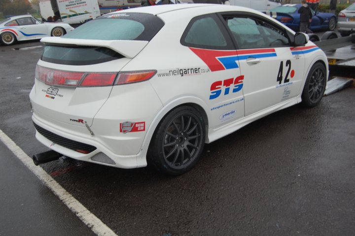 Pistonheads - In the image, there is a white car parked prominently, featuring a red and blue stripe along the side and a distinctive blue decal. The license plate of the car reads "42". The car is parked behind another vehicle, indicating a shared parking area or garage. The overall setting appears to be a parking lot or garage, as suggested by the presence of additional cars in the background. There is no visible text outside of the car's registration number. The car is facing towards the right side of the image.