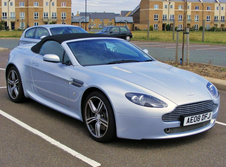 SPOTTED THREAD - Page 8 - Aston Martin - PistonHeads - The image shows a luxury convertible Aston Martin parked in a parking lot in front of residential buildings. The car has a sleek silver body with black side mirrors and the top is down. The registration on the car shows as "AE08 DJ". The car is equipped with alloy wheels, and there's a clear sky in the background.