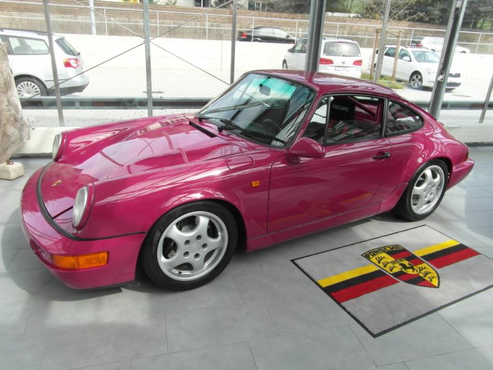 A red car is parked on the side of the road - Pistonheads - The image shows a vibrant red Porsche parked inside a building, with its front facing the camera. The car is positioned on a black and yellow striped carpet or mat, which is laid out on the concrete floor. The vehicle's design is highlighted with the iconic Porsche logo visible on the front right fender. In the background, there's a fence, suggesting either a dealership or exhibition venue.