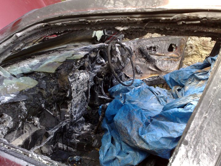 Wrong Pistonheads Welding - The image captures the interior of a wrecked car, with the roof peeled back and parts of it ripped open, revealing sharp metallic edges. A multitude of small fires are burning amidst the remains of the car, with blue plastic shredded and scattered throughout. The car appears to have been in a severe road accident, as indicated by the destruction. Smoke is visible, implying that more damage might have occurred to the vehicle prior to the image capture.