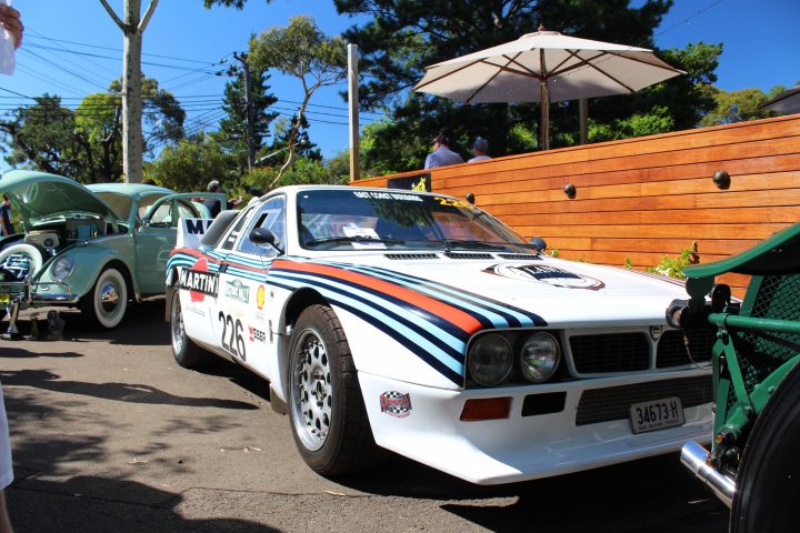 SPOTTED THREAD  - Page 14 - Australia - PistonHeads - The image showcases a white and blue rally car parked on a street next to a green vintage station wagon. The car appears to be adorned with a racing number, indicating its involvement in a rally or circuit racing program. The station wagon also exhibits a distinctive design, suggesting it might be a classic or limited edition vehicle. The setting is further enhanced with an outdoor cafe in the background, complete with shade umbrellas. The scene gives off a festive and casual atmosphere, possibly suggesting an automotive event or meet-up involving classic and rally cars.