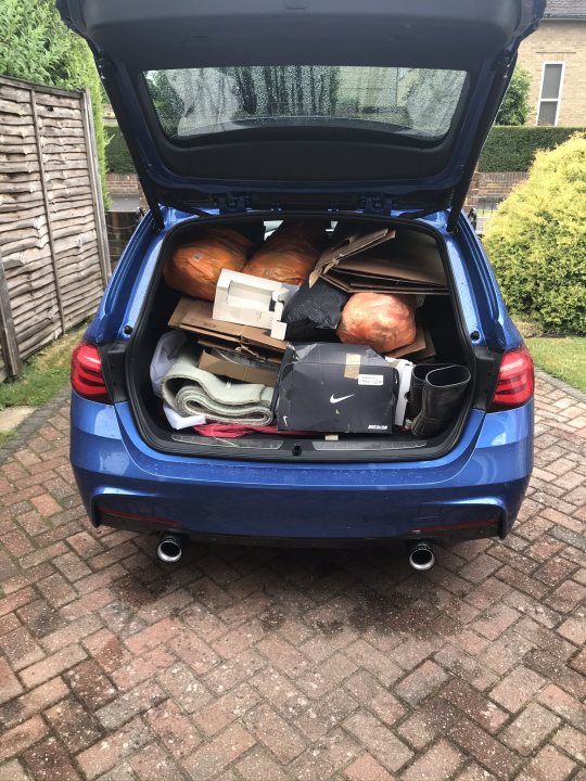 Pics of your Fast Estate... - Page 124 - General Gassing - PistonHeads UK - The image shows a blue SUV parked in front of a house. The back of the vehicle is open, revealing its cargo space filled with various items. There are at least three objects visible: what appears to be a large orange pumpkin, a stack of books or binders, and a suitcase or piece of luggage. A pair of shoes is also noticeable among the items. The car has a spare tire mounted on its rear bumper. The setting suggests that it might have been used for transporting these items, possibly related to an event or activity at the residence.