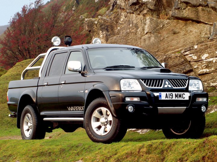 So what car have you been obsessing about today?? (Vol 2) - Page 411 - General Gassing - PistonHeads - The image presents a black Mitsubishi pickup truck parked on a grassy hillside. The truck is equipped with off-road lights on its roof, suitable for illumination in rural or uneven terrain. The context within the picture suggests a rugged outdoor location, likely beyond urban infrastructure. The car has a variety of labels indicating its model and certification, such as "A19 MMCB," "LL0" and "WARRIOR." There are some large rocks visible in the background, contributing to the overall impression of a natural, outdoorsy setting.