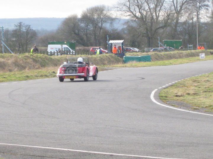 Pistonheads Sprog Porsche - This image captures a thrilling scene on a race track. The main focus is a vintage red racing car, being driven with intensity. Following close behind is a motorcycle, mirroring the speed of the car. The vehicles are on the inside of the track, emphasizing the dynamic nature of the race. The background features a verdant landscape, dotted with trees and spectators, providing a stark contrast to the high-speed action on the track.