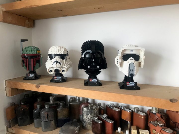 Non Technic LEGO - Page 358 - Scale Models - PistonHeads UK - The image shows a collection of Star Wars Lego head pieces arranged neatly on a shelf against a white wall. Each piece is a unique character from the Star Wars franchise, including Darth Vader and Kylo Ren, recognizable by their distinctive helmets. Below the shelf, there are items that resemble tools or parts, suggesting a crafting or repair workshop environment. The style of the image is straightforward and documentary, capturing the Lego display without any additional context.