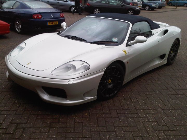 Help with a route - Page 1 - South Wales - PistonHeads - This image showcases a pristine white convertible sports car parked on a brick driveway. The vehicle's convertible top is down, and it is positioned diagonally to the viewer, with the front facing towards the top right corner of the image. The white sports car is surrounded by other parked cars, suggesting this might be a parking lot or a street side where several vehicles are parked. The brick pavement underlines the overall position and setting of the sports car. The parked cars in the background, coupled with the sports car, add a sense of depth and context to the image.